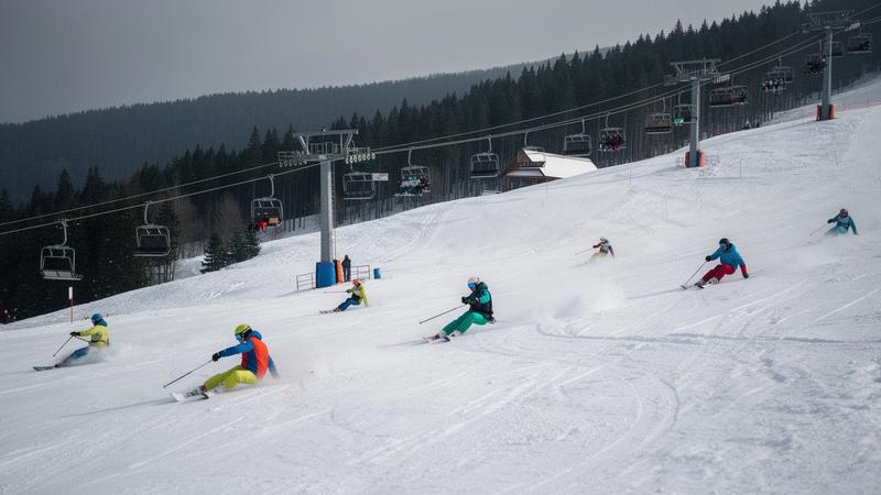 Skiers on a groomed piste in Bukovel with chairlifts and conifers behind